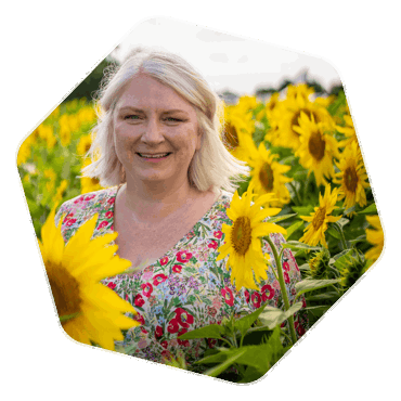 A woman with a short blonde bob, standing amongst tall sunflowers in a field.
