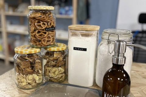 A selection of items in jars and containers from a local refill shop, there are dried fruits, washing up liquid, almonds and two types of flour on display in various containers