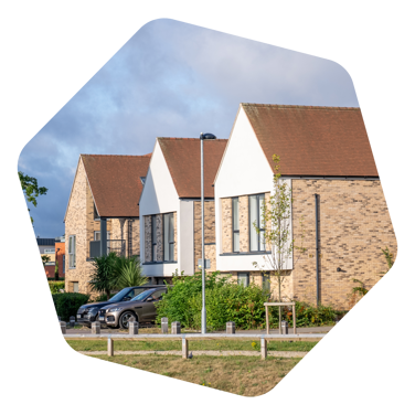 Three new modern houses in a row with two silver cars parked out front of one of the houses with some bushes out the front also