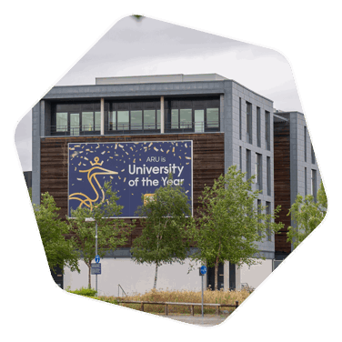 Side of an Anglia Ruskin University building with trees in the foreground. A sign on the building reads "ARU is University of the Year"